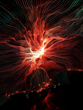 Abstract long exposure light painting with glowing red and orange fiber optic strands over rocks. Dynamic energy burst and data connection concept in dark environment. Modern artistic background.