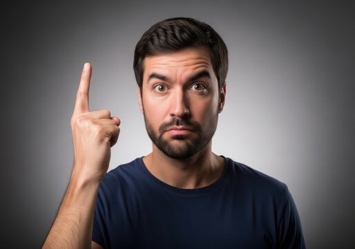 Portrait of a surprised young man with a beard pointing his finger up, expressing a sudden idea or realization against a grey studio background