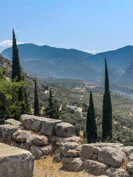 Delphi, Greece - July 23, 2024: Temple of Apollo park and ruins. Looking down into the valley. Small part of road 48. Large and wide mountain range on horizon under blue sky