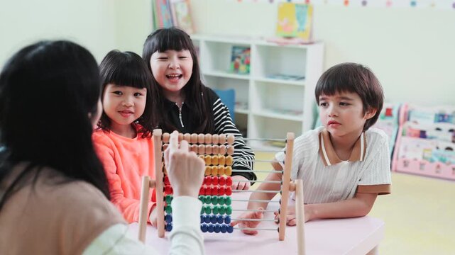 Teacher teaching children math with an abacus in kindergarten class. Asian kids learning and playing with educational toys in preschool daycare room, early childhood development.