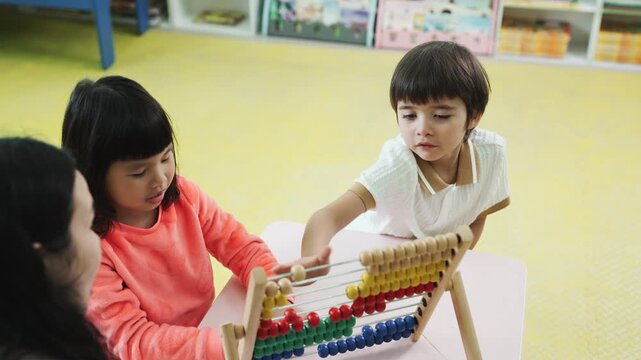 Teacher teaching children math with an abacus in kindergarten class. Asian kids learning and playing with educational toys in preschool daycare room, early childhood development.