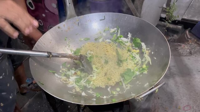 Cooking traditional Indonesian stir fried noodles or mie goreng in a large wok