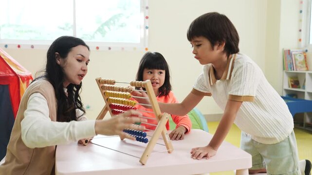 Teacher teaching children math with an abacus in kindergarten class. Asian kids learning and playing with educational toys in preschool daycare room, early childhood development.