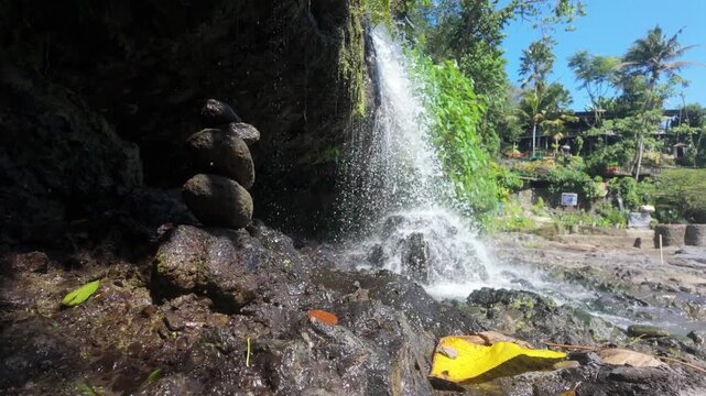 Small hidden waterfall located at the top of Tegenungan waterfall in Ubud, Bali. Slow motion push in. A rock cairns / tower sits next to the water. 