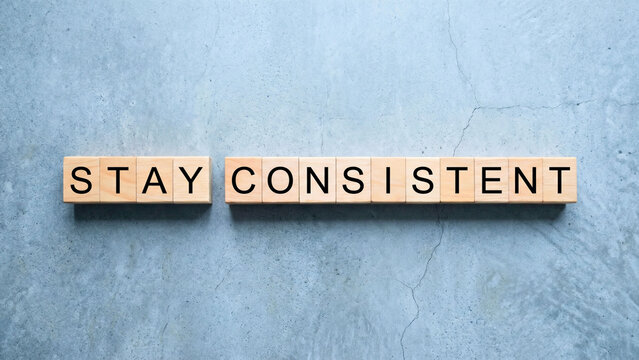 Wooden blocks spelling Stay Consistent on grey concrete surface overhead, consistency success concept, long term goal achievement, disciplined action principle professional