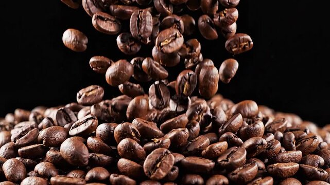 Roasted aromatic brown coffee beans falling in slow motion onto a pile of fresh coffee beans isolated on a dark black background for breakfast energy