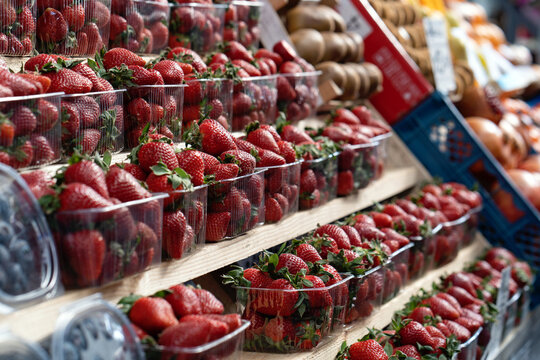 Fresh, ripe, large red strawberries with green leaves in a plastic container or box neatly displayed on a counter at a street fruit and vegetable market. Close up.