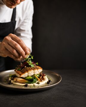Chef garnishing a gourmet fish dish on a restaurant plate