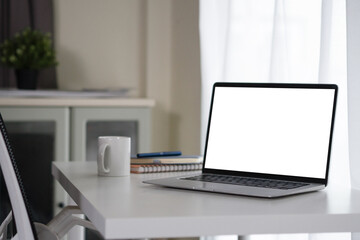 Fototapeta premium Laptop with Blank White Screen on Clean White Desk in Modern Home Office Workspace with Coffee Mug and Notebook