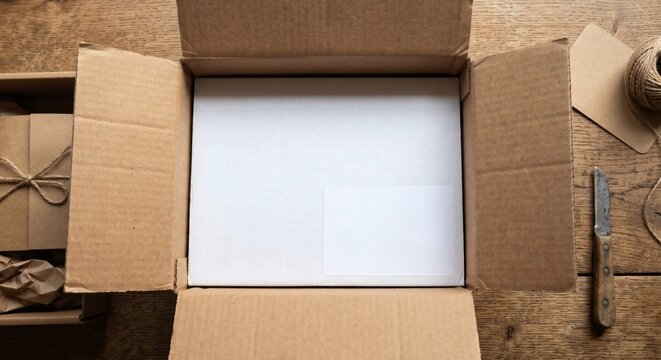 Blank white shipping label mockup inside open cardboard box top down POV