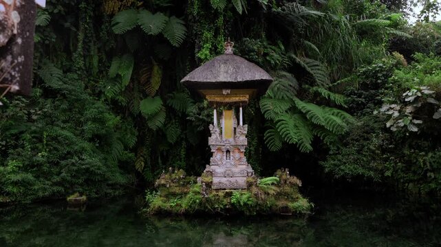 Small Balinese Hindu pelinggih shrine sit's on the water with a backdrop of jungle and crystal clear water. Location: Pura Gunung Kawi Sebatu Water Temple, Ubud, Bali.