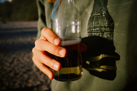 Person holding a bottle of beverage on the beach during sunset