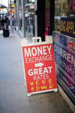 money exchange sign with currency symbols on city sidewalk