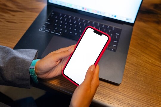 Person holding phone next to laptop at a desk