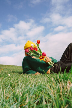 Woman holding flowers while lying on grass under the sky