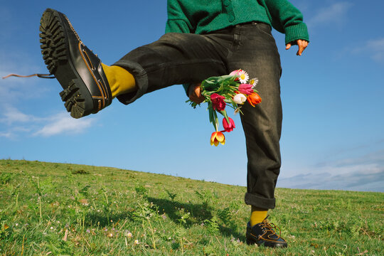 Person holds flowers while standing on grass in bright weather