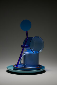 Abstract composition of blue glass objects and ceramic mug on a plate