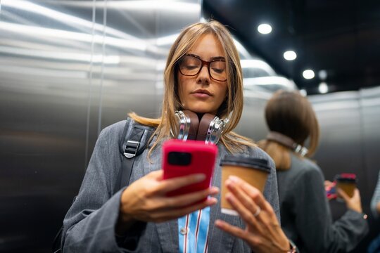 Woman using phone in elevator with coffee cup