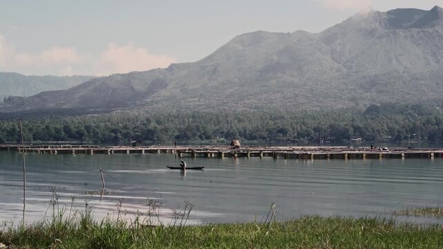 Scenic view of Mount Batur from Batur lake. Isolated by cloudy sky. There is fisherman and tilapia fish or ikan mujaer's cage. 4K Horizontal timelapse footage. Tavel, nature concept