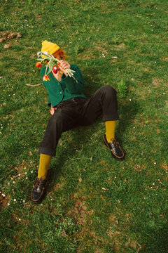 Person sits on grass holding flowers in hand with bright colors