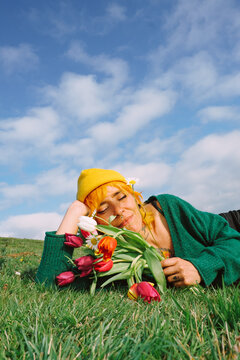 Woman lying on green grass holding flowers under blue sky