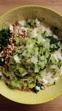 Adding Cooked Vegetables To Spinach Feta Bowl Top View Vertical