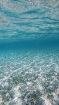 Crystal blue ocean underwater and sandy sea bottom with waves on surface