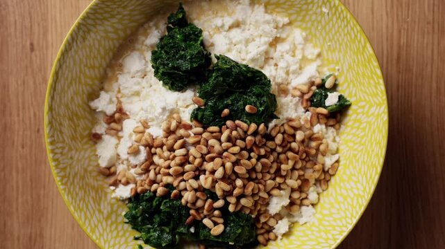 Adding Pine Nuts To Spinach Feta Bowl Top View