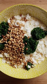 Adding Pine Nuts To Spinach Feta Bowl Top View Vertical