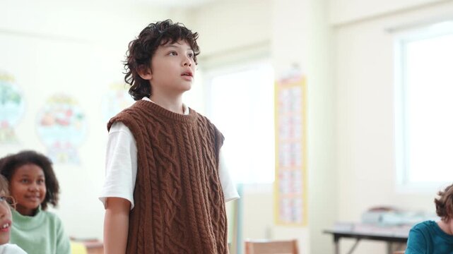 Confident boy standing and speaking to introduce himself in classroom. Elementary school student giving a presentation during a diverse learning lesson.