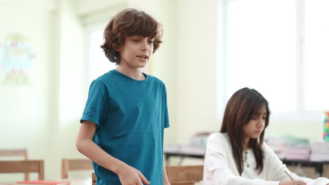 Confident boy standing in classroom speaking and giving a presentation. Elementary student introducing himself and sharing his hobby during a school lesson.
