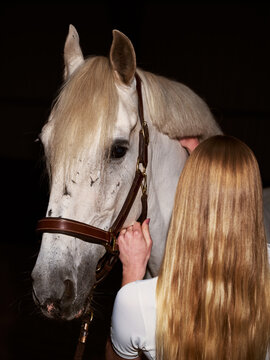 Woman Interacts With White Horse in Dimly Lit Stable