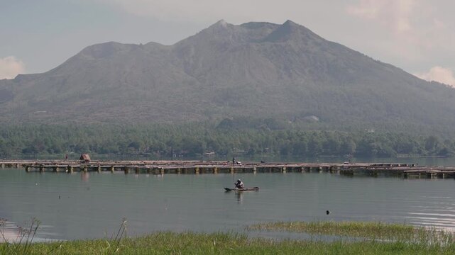 Scenic view of Mount Batur from Batur lake. Isolated by cloudy sky. There is fisherman and tilapia fish or ikan mujaer's cage. 4K Horizontal timelapse footage. Tavel, nature concept
