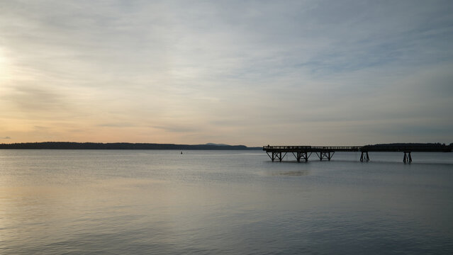 Sunset over calm water with a pier in the distance