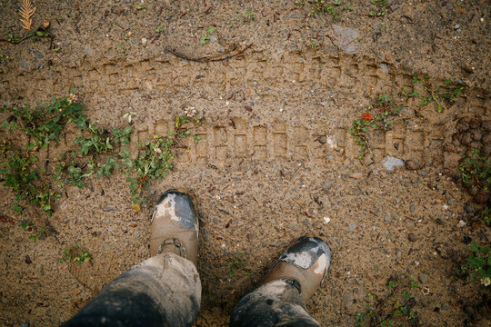 Boots on muddy ground showing dirtbike tire tracks and grass