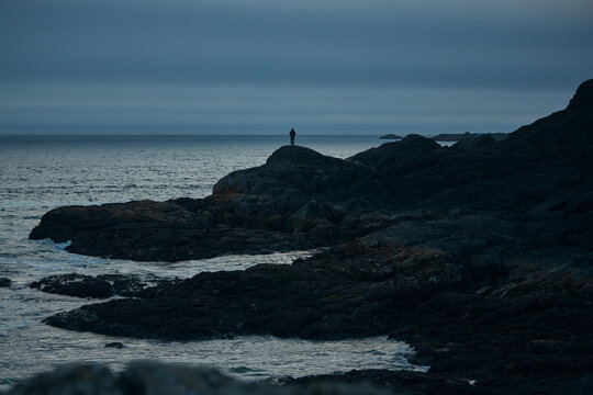 People stand on rocks by the ocean during sunset at a coastal location