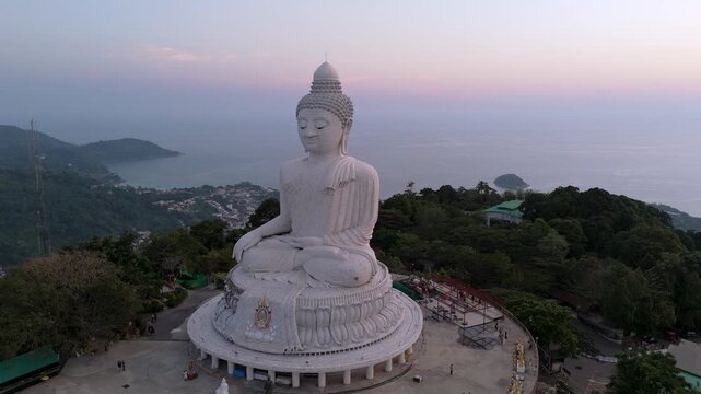 Aerial top sunset view magnificent white marble Buddha statue sits serenely atop a lush Phuket hilltop