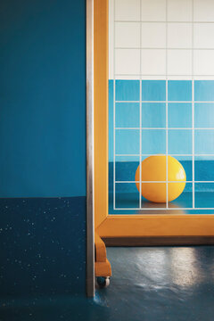 Reflection of a right Yellow Ball Sits in a Room With Blue Walls 