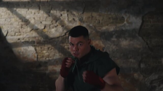 Determined young boxer practicing shadow boxing in dark industrial gym. Male fighter training punches and movement in cinematic moody ligh