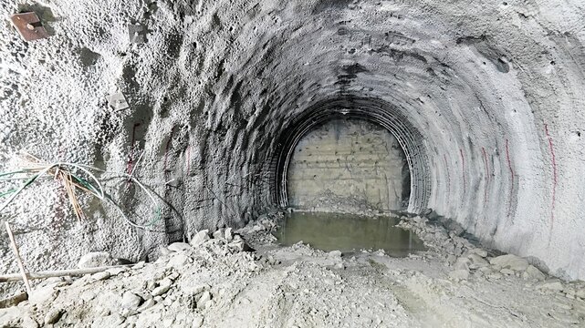 View of a tunnel construction site with raw concrete walls, exposed steel reinforcement, and a pool of water on the ground in Karabuk, Karabuk, Turkiye.