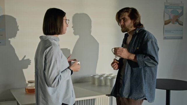 Caucasian young woman and Caucasian young man standing and talking during support group break, holding mugs. Clip for mental health awareness campaigns and therapy services