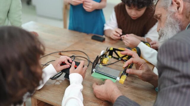 Close up of teacher hands pointing finger up explaining robot idea. Diverse students learning STEM science and engineering project together in elementary school.