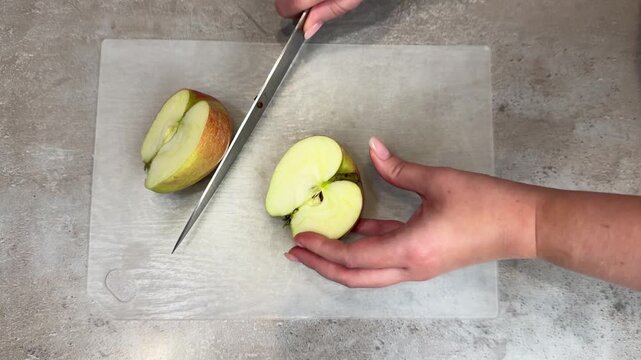 Hands slicing green apple on cutting board mid sequence showing downward knife motion and food prep