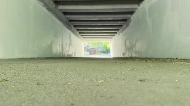 A cyclist rides through a concrete underpass toward the bright exit. The movement creates a sense of freedom and energy as they transition from the shadows into the day.