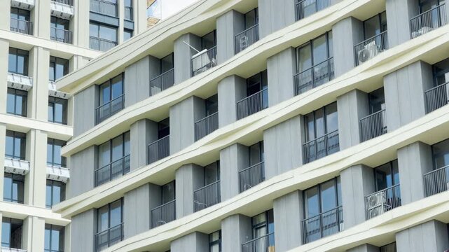 A modern apartment building displays a repeating pattern of geometric balconies and glass windows. The crisp architecture creates a sense of orderly calm in the city environment.