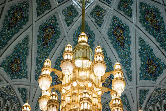 View of the ornate golden chandelier hanging from the intricately tiled dome ceiling inside the Sultan Qaboos Grand Mosque in Muscat, Muscat Governorate, Oman.