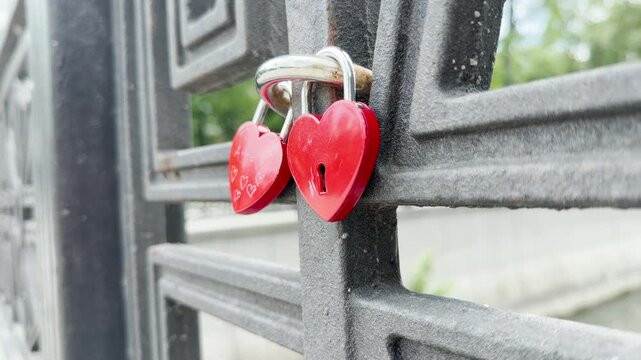 Two red heart-shaped padlocks are locked tightly onto a metal bridge railing. They represent a couple's eternal love, romantic hope, and joyful commitment.