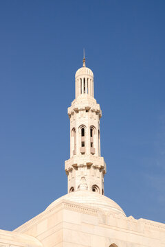 View of the ornate white stone minaret of the Sultan Qaboos Grand Mosque against a clear blue sky in Muscat, Muscat Governorate, Oman.