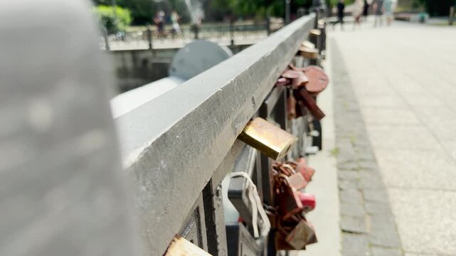 Multiple wedding padlocks hang on a metal bridge railing. The rusty locks symbolize eternal love and commitment. This sweet scene brings a romantic and hopeful feeling.