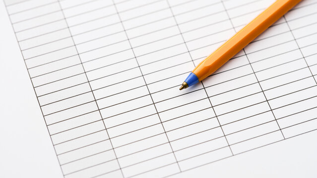 An orange ballpoint pen lying on a blank paper table grid document. Close up.